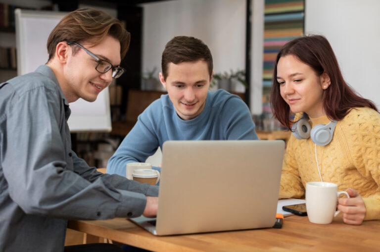 Three individuals sitting at a table with a laptop, discussing methods to accelerate young professionals' career development.